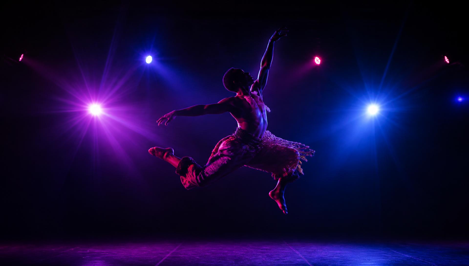Dancer leaping on a stage lit with purple, blue and pink lights